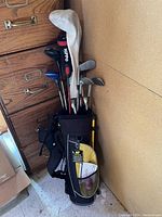 Full view of golf bag with multiple left hand golf clubs inside, wooden furniture in background