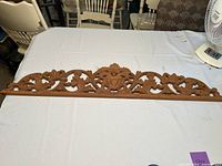 Full view of the wood carved wall hanging showing overall length and intricate scrollwork design.