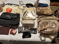 Full assortment of purses and wallets laid out on a bed, showing variety of colors and styles including metallic, fabric, and leather items.