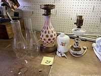 Overview photo showing both lamps side by side on a wooden surface, including additional glass chimneys and a broken porcelain lamp shade.
