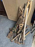 Pile of antique and vintage tools including saws, hammers, axes, garden tools shown resting against cabinet