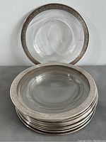 Stack of ten clear glass plates each with a sterling silver engraved rim, one plate standing upright behind.