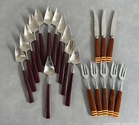 Set of 8 Rostfrei Solingen Art Deco knives with maroon handles and 12 Pierre Forsell cocktail forks with wooden striped handles laid flat showing overall lot contents