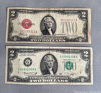 Fronts of two U.S. $2 bills showing portraits of Thomas Jefferson, one with a red Treasury seal and one with a green seal, both showing significant wear and creases.