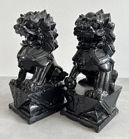 Pair of black painted stone statues of Chinese Beijing lions/Fu Foo dogs angled front left.