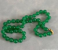 Photo showing the full necklace laid out on a flat surface highlighting the green beads and gold-tone clasp.
