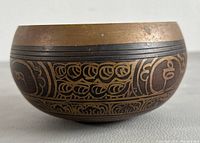 Side view of Tibetan singing bowl showing engraved traditional patterns in copper and dark metallic finish.