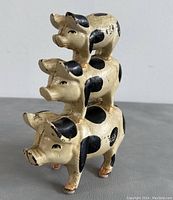 Front view of the vintage cast iron stacked pigs doorstop, showing three pigs vertically stacked with cream color and black spot patterns.