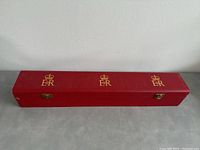 Top view of the closed red scroll box with three gold 'E II R' and crown insignia evenly spaced along the length of the box.