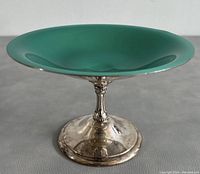 Side view of the pedestal plate showing the green enamel top and silver plated pedestal base with minor surface wear.