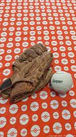 Left-handed brown leather baseball glove positioned alongside a Cooper branded baseball on an orange and white patterned background.