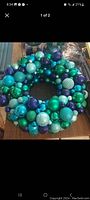 Photo of a holiday wreath made of assorted Christmas ball ornaments in various green, blue, teal, and purple hues placed on a wooden surface.