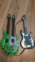 Set of two Kawasaki electric toy guitars, close-up front view on wooden floor.
