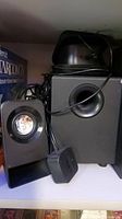 Full view of the subwoofer and one satellite speaker with cables visible, dark black color, rectangular shapes with round ports.