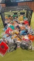 Photo of large number of McDonald's toys in original sealed plastic bags in front of a black crate on a green table.