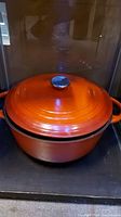 Front view of orange Dutch oven pot with lid, showing silver knob and side handles.