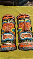 Front view of two colorful plastic tiki head wall decorations showing detailed paint and patterns.