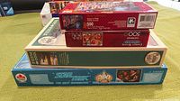 Four jigsaw puzzles stacked, showing puzzle piece counts and box designs.