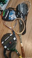 Photo showing four racquets placed on the floor along with a black Head racquet carry bag with tennis player image.
