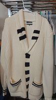Front view of vintage chunky knit curling sweater showing cream main color with black stripes on collar, button placket and pockets.