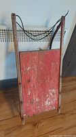 Front view of vintage sled showing red painted wood panel with rope handle and wooden frame.