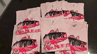 Seven folded pink women's t-shirts with a walleye fish graphic on front and 'Walleye' text, in various sizes.