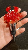Front view of glass crab stopper showing the red crab with white spots and black eyes mounted on metal stopper with rubber ring