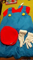 Red shirt, blue overalls with yellow buttons, red Mario hat and white gloves shown together on a surface.