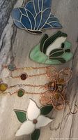 Photo showing four decorative window hangers including three stained glass flowers and one metal butterfly with hanging beads.