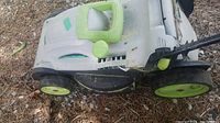Side view of the Lawnmaster electric lawnmower showing green wheels and lightweight plastic body, placed on dry ground.