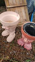 Two garden pots with funny face and foot designs, placed outdoors on leaf-covered ground.