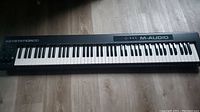 Full view of the M-Audio Keystation 88-key MIDI keyboard on floor showing all 88 keys and branding.