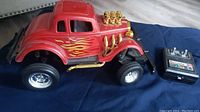 Full view of red vintage Ford Hot Rod toy with flame decals and gold engine showing attached wired remote control