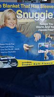 Box front showing Snuggie blanket branding, features, and image of person wearing the blanket.