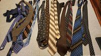 Top view of ten men's neckties arranged side by side on a light surface showing a variety of patterns and colors.