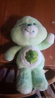 Front view of green plush bear with four-leaf clover on stomach, showing entire bear.
