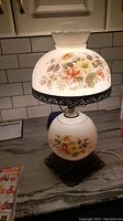 Full view of vintage 22-inch hurricane table lamp with floral decorated glass globe base and matching scalloped globe shade on ornate metal base.