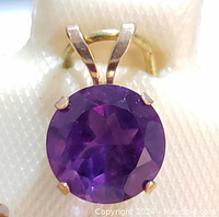 Close-up photo of the pendant showing the round cut deep purple amethyst held by four yellow gold prongs.