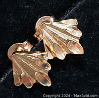 Close-up image of one earring showing the ridged fan or meteor-inspired design in yellow gold on a black background.