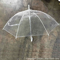 Photo of one clear transparent umbrella opened on floor showing large dome canopy, white ribs, shaft, and J-handle