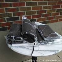 Four brown high density foam chair cushions with tie-down straps displayed on a round marble table. Two cushions are wrapped sealed in plastic, two are unwrapped and appear unused.