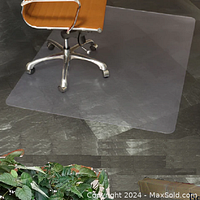 Clear rectangular chair mat under office chair on dark textured hard floor.