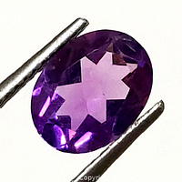 Close-up image of oval faceted natural amethyst held by gem tweezers showing front face with vivid purple hues.
