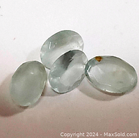 Four oval light blue natural aquamarine gemstones shown from top and side angles revealing transparency, polish, and minor inclusions.