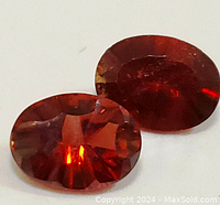 Close-up image of two oval faceted garnet gemstones showing deep red color and light reflections.