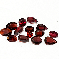 Close-up of multiple natural red garnet gemstones in various faceted cuts and deep red color.
