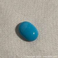 Close-up image of the polished oval turquoise gemstone on fabric background showing the bright medium blue color and smooth surface.