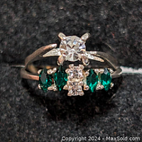 Top view of two 925 silver rings; one ring has a single large clear CZ stone flanked by green garnets and small clear stones, the other ring with multiple green garnet and clear CZ stones.