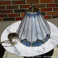 Side view of conical stained glass ceiling light showing white marbled and blue leaf motif stained glass panels with metal leaded trim and antique brass hanging chain and ceiling mount.