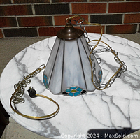 Full view of the stained glass swag lamp with chain and power cord on a marble surface outside, showing the lampshade with white marbled panels and blue flower motifs.